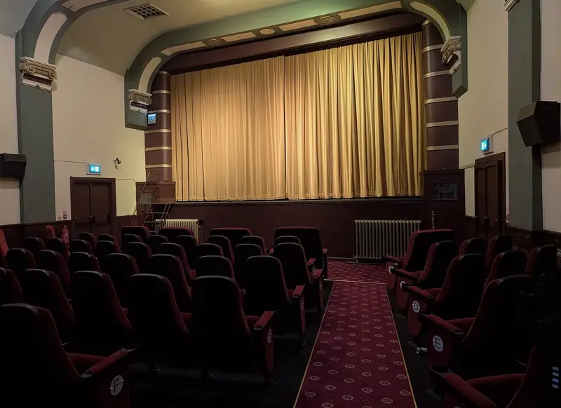 Salle de cinéma aux fauteuils rouges, rideau doré tiré devant l'écran